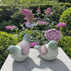 To stribede keramikfugle i rosa og gr�nne farver placeret i et blomstrende havemilj�. Fuglene st�r i dagslys og viser deres frostsikre glasur.