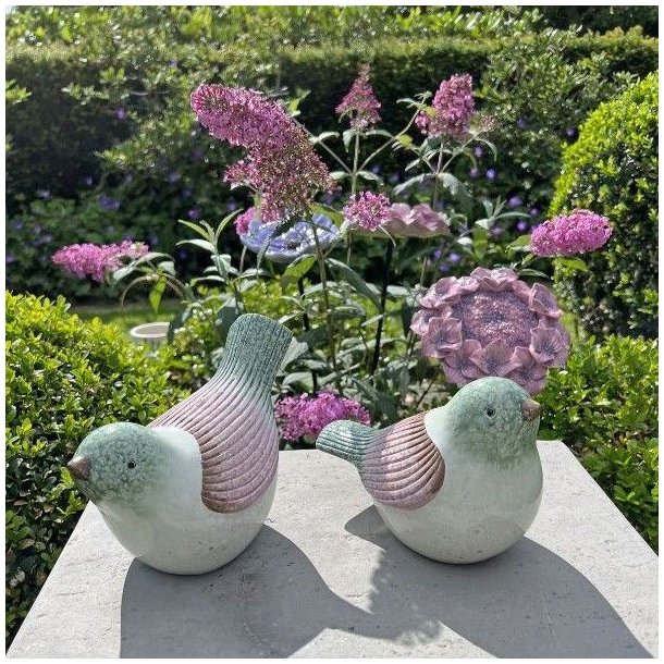 To stribede keramikfugle i rosa og gr�nne farver placeret i et blomstrende havemilj�. Fuglene st�r i dagslys og viser deres frostsikre glasur.
