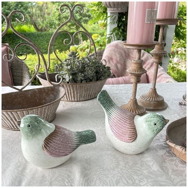 To varianter af de stribede keramikfugle i rosa og gr�nne nuancer vist sammen i et lyst milj�. Begge fugle er frostsikre og m�ler H14/L19 cm.