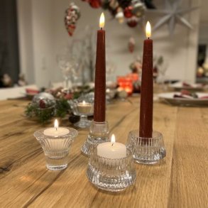 Klare rillede glasfyrfadsstager og lysestager med r�dbrune kronelys placeret p� et d�kket tr�bord i julestemning.