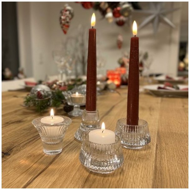 Klare rillede glasfyrfadsstager og lysestager med r�dbrune kronelys placeret p� et d�kket tr�bord i julestemning.