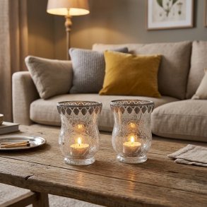 Stemningsfuldt milj�billede med 2 krakelerede fyrfadsstager i glas med s�lvkant, placeret med t�ndte fyrfadslys p� et sofabord i en hyggelig stue.