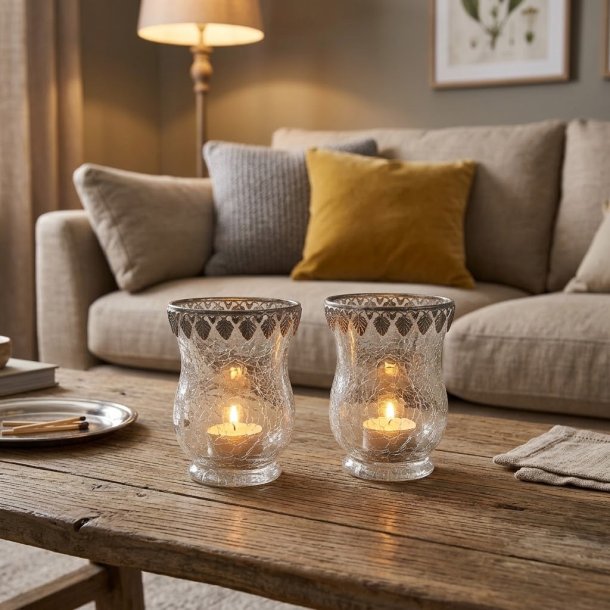 Stemningsfuldt milj�billede med 2 krakelerede fyrfadsstager i glas med s�lvkant, placeret med t�ndte fyrfadslys p� et sofabord i en hyggelig stue.