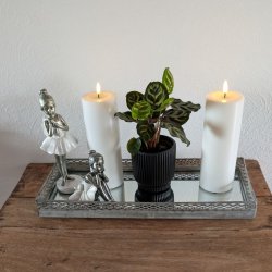 Stemningsfuldt firkantet milj�billede af det hvide LED-bloklys med t�ndt real flamme, st�ende p� en dekorativ spejlbakke med figurer og en gr�n plante p� et tr�bord.