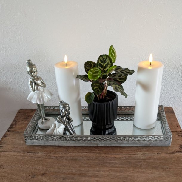 Stemningsfuldt firkantet milj�billede af det hvide LED-bloklys med t�ndt real flamme, st�ende p� en dekorativ spejlbakke med figurer og en gr�n plante p� et tr�bord.