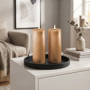 Stemningsfuldt firkantet milj�billede af de karamelbrune LED-bloklys med t�ndte real flammer fra Deluxe Homeart, placeret p� en sort rund bakke p� en hvid sk�nk i en hyggelig stue.