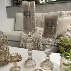 To h�je champagnefarvede La Vida glasstager med beige bloklys st�ende p� et bord i en stue.