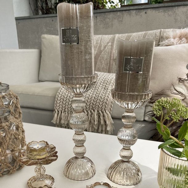 To h�je champagnefarvede La Vida glasstager med beige bloklys st�ende p� et bord i en stue.