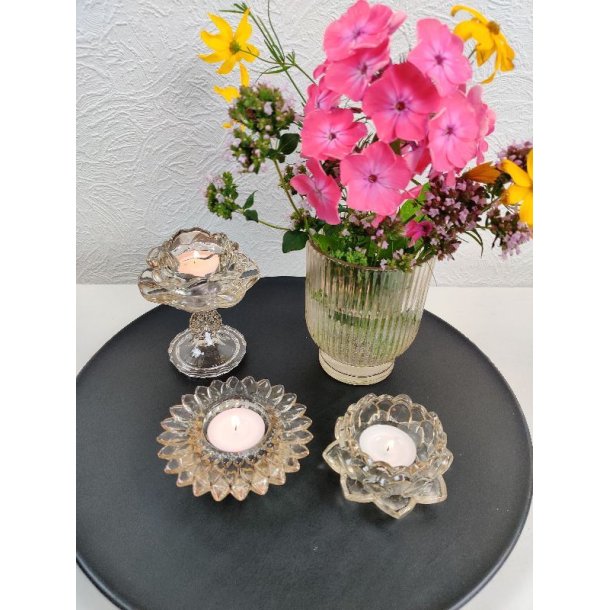 Champagnefarvede fyrfadsstager i glas fra La Vida med t�ndte lys og en blomstervase p� en m�rk bakke.