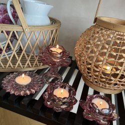 Fire rosa farvede La Vida fyrfadsstager i glas formet som blomster og lotusstager med t�ndte lys placeret ved en fletlanterne og kurv.