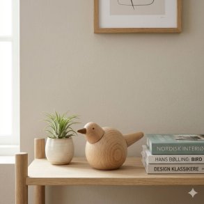 Et kvadratisk livsstilsbillede af den lyse tr�fuglfigur fra La Vida, der st�r p� en lys egetr�shylde. Fuglen er udf�rt i lyst egetr� og m�ler tretten centimeter i h�jden og elleve centimeter i l�ngden. Den st�r sammen med en lille hvid keramikpotte med en luftplante og en stabel p� tre b�ger i et moderne nordisk interi�r. Naturligt dagslys oplyser scenen.