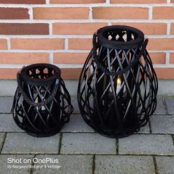 Rund fletlanterne i naturfarvet rattan med en praktisk hank og en gennemsigtig glascylinder til lys indeni, vist p� en lys baggrund.