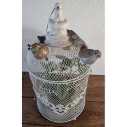 N�rbillede af et hvidt lanternebur i metalnet dekoreret med to sm� glitrende pyntefugle. Indeni buret ses en gr�n plante og en fin lysk�de, der skaber en hyggelig atmosf�re.