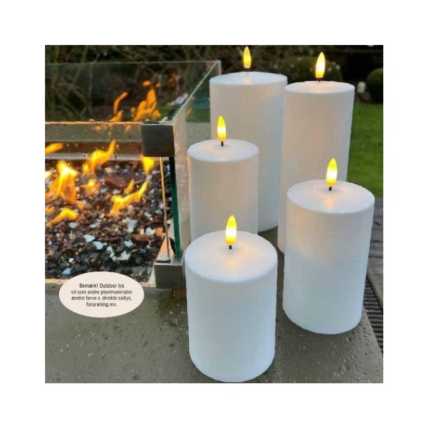 Et hvidt udend�rs LED-bloklys med en varm, t�ndt flamme placeret i en rustik lanterne p� en tr�terrasse i skumringen.