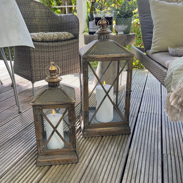 To store lanterner med hvide udend�rs LED-bloklys placeret p� en hyggelig tr�terrasse sammen med havem�bler.