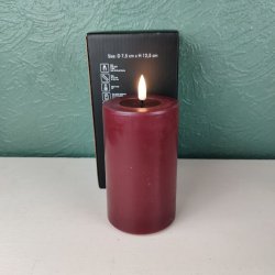 Milj�billede af det t�ndte bordeauxfarvede LED-bloklys p� D 7,5 cm x H 12,5 cm st�ende foran den tilh�rende sorte produkt�ske.