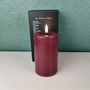 Milj�billede af det t�ndte bordeauxfarvede LED-bloklys p� D 7,5 cm x H 12,5 cm st�ende foran den tilh�rende sorte produkt�ske.