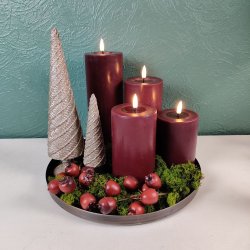 Stemningsfuldt overbliksbillede af en jule- og adventsdekoration p� et rundt fad med bordeaux LED-bloklys, glitrende dekorative juletr�er i guld, gr�nt mos og b�r.