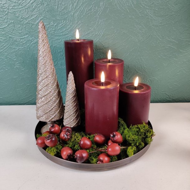 Stemningsfuldt overbliksbillede af en jule- og adventsdekoration p� et rundt fad med bordeaux LED-bloklys, glitrende dekorative juletr�er i guld, gr�nt mos og b�r.