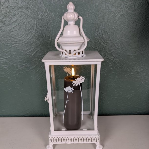 Stemningsfuldt milj�billede af det mokkabrune LED-bloklys med t�ndt real flamme fra Deluxe Homeart, placeret indeni en hvid metal- og glaslanterne dekoreret med hvide blomstermotiver.