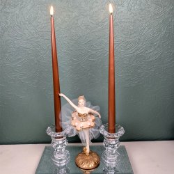 Milj�billede af to t�ndte brune LED-stagelys placeret i fine glaslysestager p� en spejlbakke med en ballerinafigur i midten foran en gr�n strukturv�g.