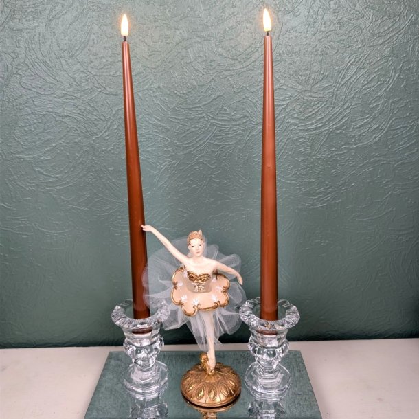 Milj�billede af to t�ndte brune LED-stagelys placeret i fine glaslysestager p� en spejlbakke med en ballerinafigur i midten foran en gr�n strukturv�g.