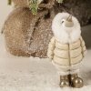 Et n�rbillede, der fokuserer p� den lille variant (H13,5 cm) af pingvin-figuren. Billedet viser de fine detaljer i dens beige dunjakke med hvid pelshals og dens statement-guldst�vler mod en rustik tr�kasse.