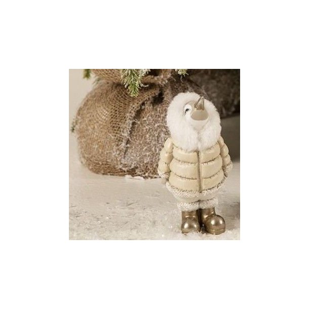 Et n�rbillede, der fokuserer p� den lille variant (H13,5 cm) af pingvin-figuren. Billedet viser de fine detaljer i dens beige dunjakke med hvid pelshals og dens statement-guldst�vler mod en rustik tr�kasse.