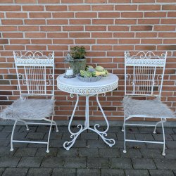 Et s�t af to hvide caf�stole i metal med matchende lysegr� imiterede lammeskindshynder, opstillet omkring et lille hvidt havebord mod en murstensv�g.
