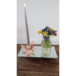 En dekorativ opstilling p� en spejlbakke med sommerfugle-lysestagen og et lilla kronelys ved siden af en lille glasvase med p�skeliljer og perlehyacinter.