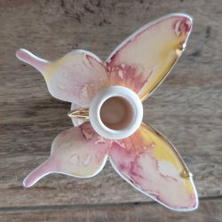 En lysestage i porcel�n formet som en sommerfugl set direkte fra oven. Vingerne har smukke akvarel-nuancer i lyser�d, gul og lilla med fine guldkanter.