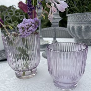 To lavendelfarvede Marly fyrfadsstager og vaser i rillet glas opstillet udend�rs p� et hvidtd�kket bord med blomster.
