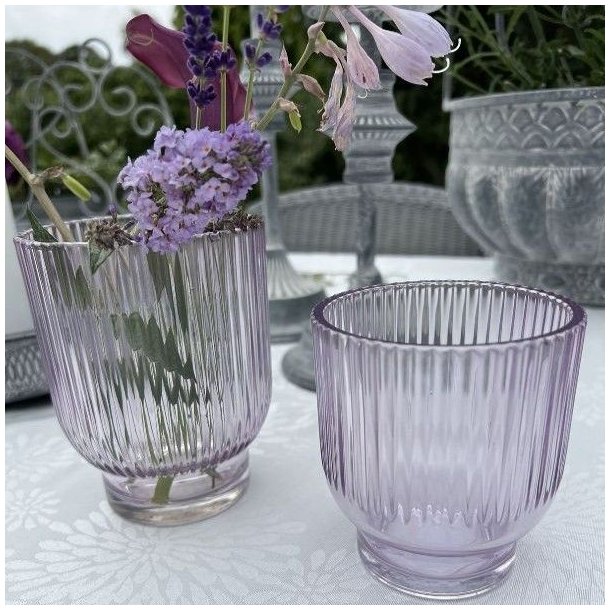 To lavendelfarvede Marly fyrfadsstager og vaser i rillet glas opstillet udend�rs p� et hvidtd�kket bord med blomster.