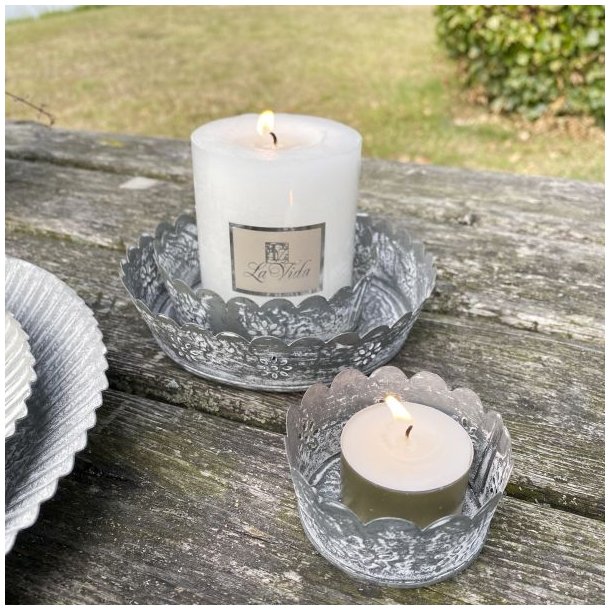 Antik gr� metalfade i to st�rrelser med t�ndt hvidt bloklys og fyrfadslys placeret p� et rustikt tr�bord.