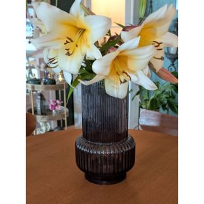 M�rkegr� rillet retro glasvase med en stor buket gule liljer placeret p� et rundt spisebord i tr�.