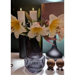 N�rbillede af en m�rk rillet glasvase i retrodesign fyldt med liljer, st�ende i hyggelig belysning ved siden af levende lys.