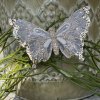Champagnefarvet organza sommerfugl med glimmer og clips fastgjort p� gr�nne grene foran en m�nstret urtepotte.