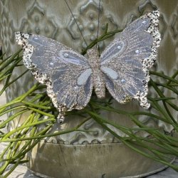 Champagnefarvet organza sommerfugl med glimmer og clips fastgjort p� gr�nne grene foran en m�nstret urtepotte.