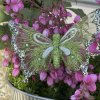 Gr�n organza sommerfugl med clips, hvide aftegninger og similisten sat p� en potteplante med sm� lyser�de blomster.