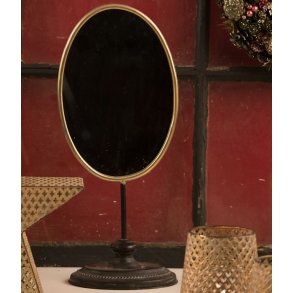Ovalt bordspejl med tynd guldkant p� en h�j sort fod (H53,5 cm) placeret i en hyggelig indretning.