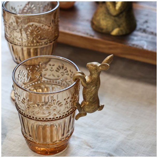 Lille p�skehare i guld-finish der h�nger dekorativt p� kanten af et drikkeglas.
