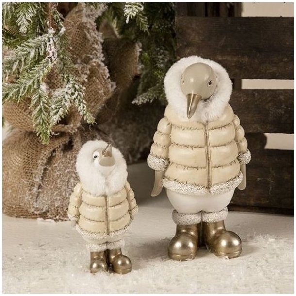 Et stemningsfuldt milj�billede, der viser de to tilg�ngelige varianter af de detaljerede pingvin-figurer. Den store (H20,5 cm) og lille (H13,5 cm) pingvin st�r i kunstig sne. De s�lges enkeltvis og assorteret. De b�rer beige dunjakker og skinnende guldst�vler.