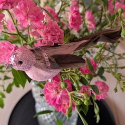 Sidel�ns n�rbillede af en 15 cm lang rosabrun dekorationsfugl med m�rke naturfjer og glitrende detaljer i en rosenbuket.