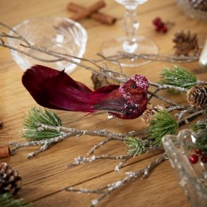 R�d dekorationsfugl med glimmer placeret p� en gren i en hyggelig juledekoration med grankogler og kanelst�nger p� et tr�bord.