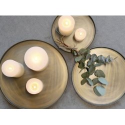 runde-messingbakker-detalje-lys Milj�billede af de runde bakker med antik messing-finish placeret p� en gr� overflade. Bakkerne er dekoreret med hvide bloklys i forskellige h�jder og en lille gren, hvilket fremh�ver deres rustikke patina.