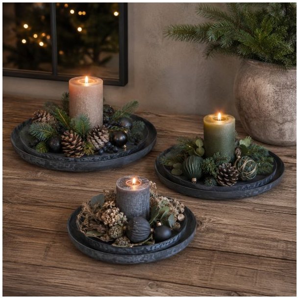 Runde sorte metalfade opstillet som hel�rsdekorationer med bloklys, gran og kogler p� et tr�bord.