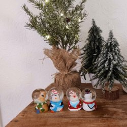 Stemningsfuldt milj�billede af fire sm� rystekugler med snemand, julemand, rensdyr og pingvin opstillet ved siden af juletr�er og juledekorationer