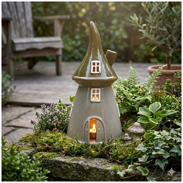 Eventyrligt keramikhus med gr�nt tag placeret i haven med t�ndt lys. Skovhuset er omgivet af planter og mos p� en terrasse, hvilket skaber en hyggelig stemning som fyrfadsstage.