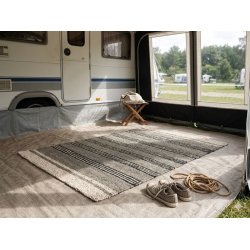 Et rektangul�rt s�gr�st�ppe med sorte striber og lyse kanter i m�lene 120x180 cm er placeret i et lyst fortelt til en campingvogn T�ppet fungerer som en praktisk og stilfuld l�ber der skaber en hyggelig atmosf�re i camping-milj�et sammen med afslappet tilbeh�r som sko og reb