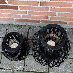 En oppefra-og-ned-visning af to sorte fletlanterner p� en terrakotta-flise, med synlige glasindsatser.